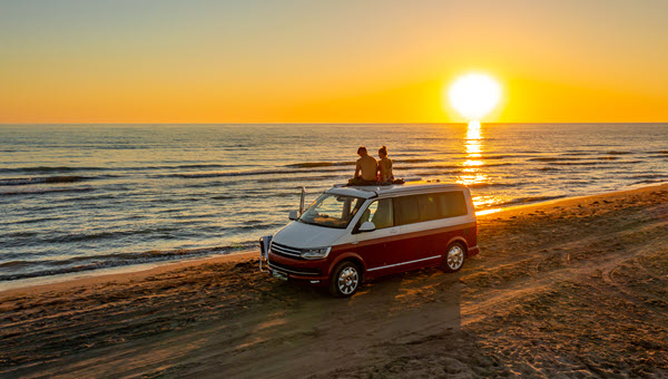 Couple sitting on a campervan on the beach at sunset
