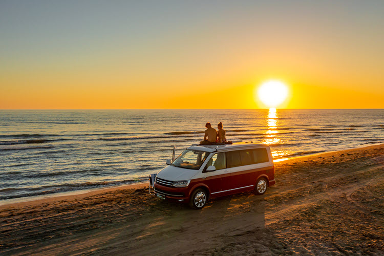 Couple sitting on campervan on a beach at sunset