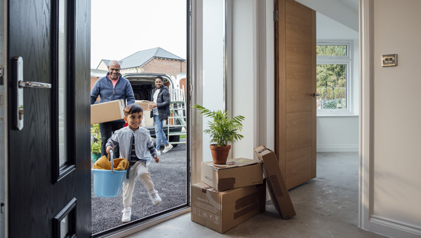 Family moving into new home with boxes and plant near open front door.