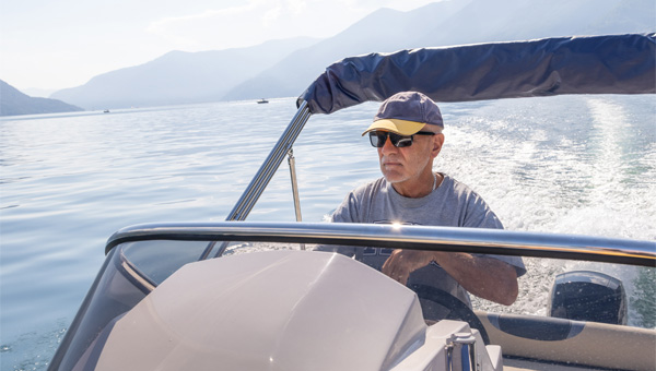 Person steering boat on water with mountains in background.