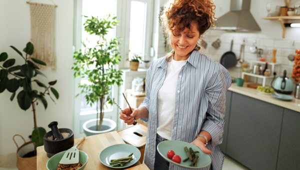 Person holding plate of food in kitchen with plants and utensils in background.
